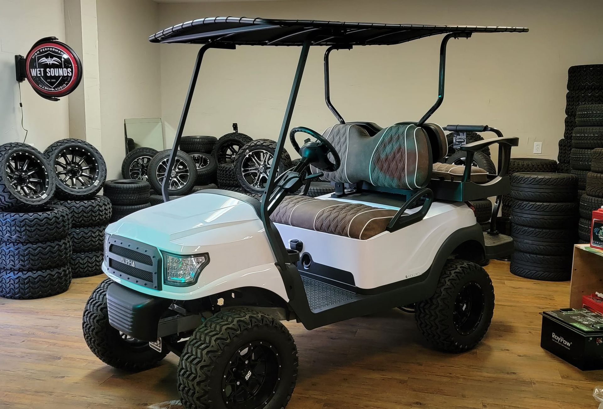 A white golf cart is parked in a room filled with tires.