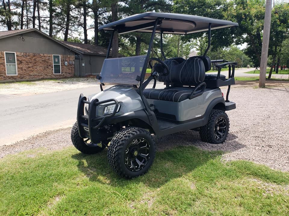 A golf cart is parked in the grass in front of a house.
