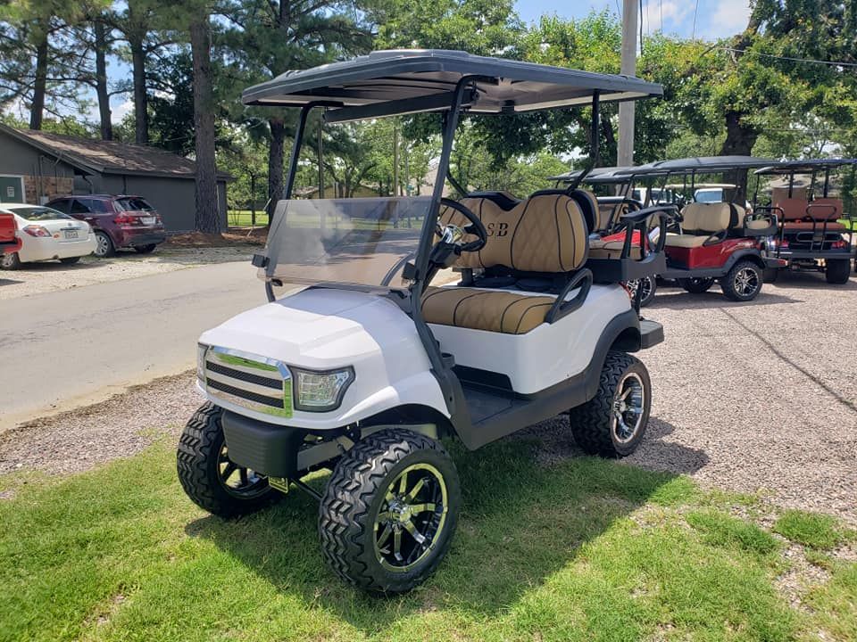 A white golf cart is parked on the grass in a parking lot.