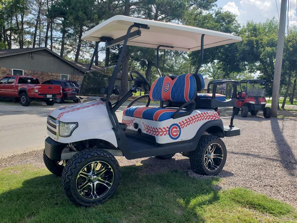 A white golf cart with blue and orange seats is parked in the grass.