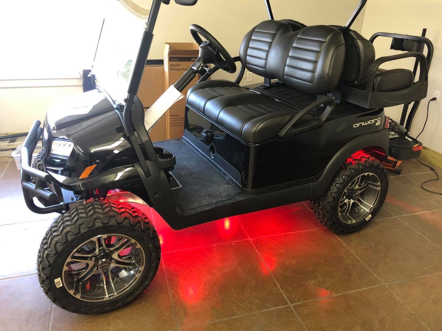 A black golf cart with red lights on the wheels is sitting on a tiled floor.