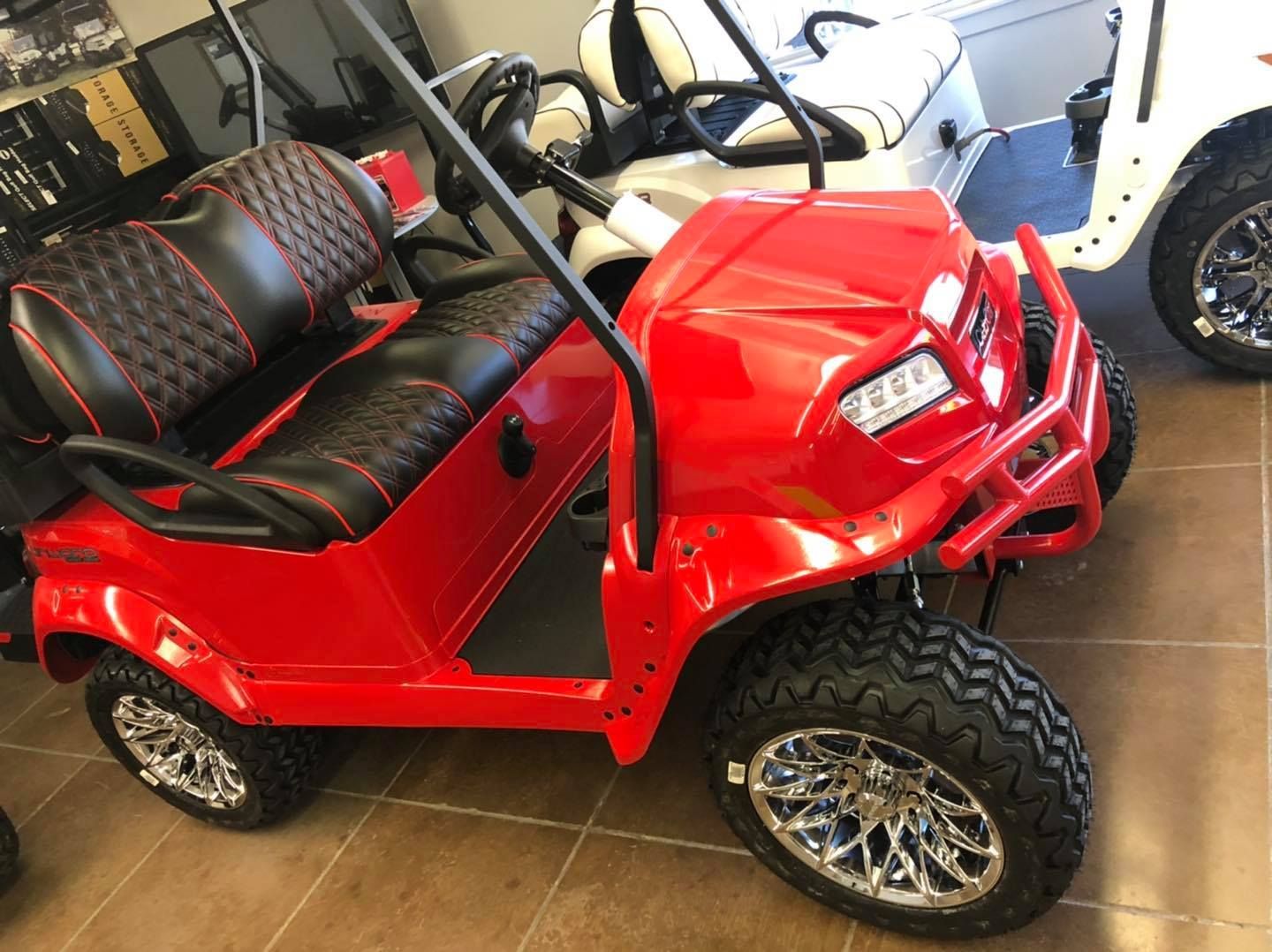 A red golf cart is parked next to a white golf cart in a showroom.