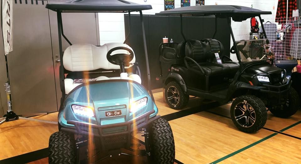Two golf carts are parked next to each other on a wooden floor.