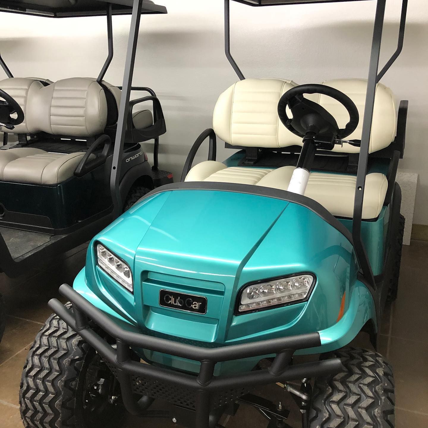 A green golf cart with white seats is parked in a garage.