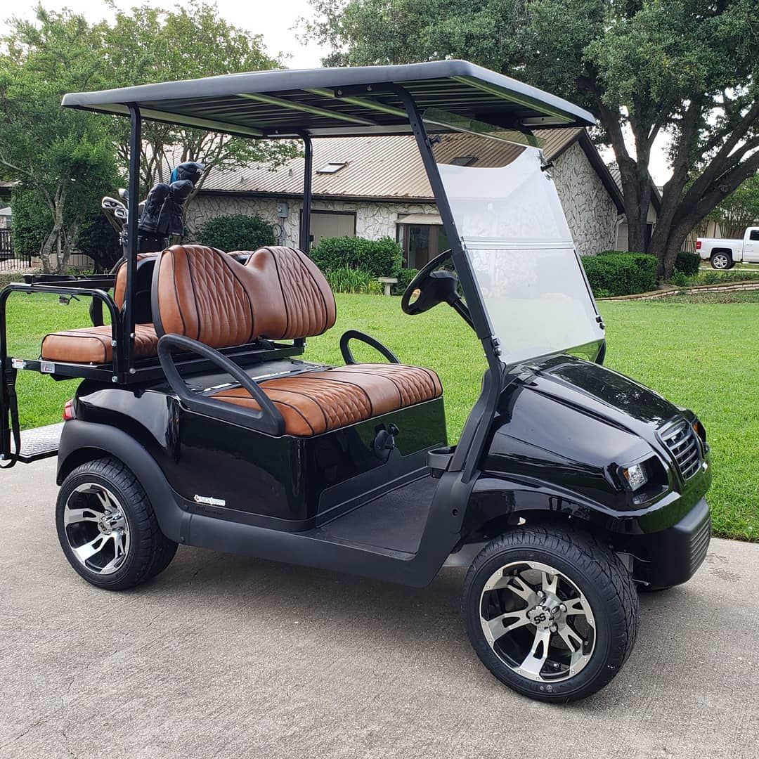 A black golf cart with brown seats is parked in front of a house.