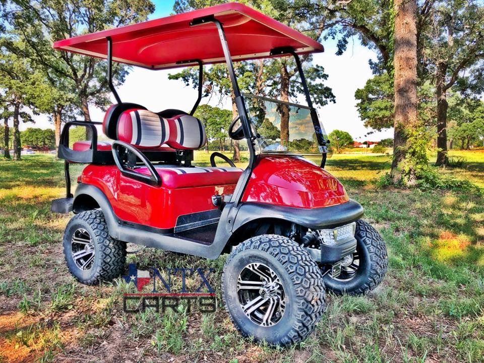 A red golf cart is parked in a grassy field.