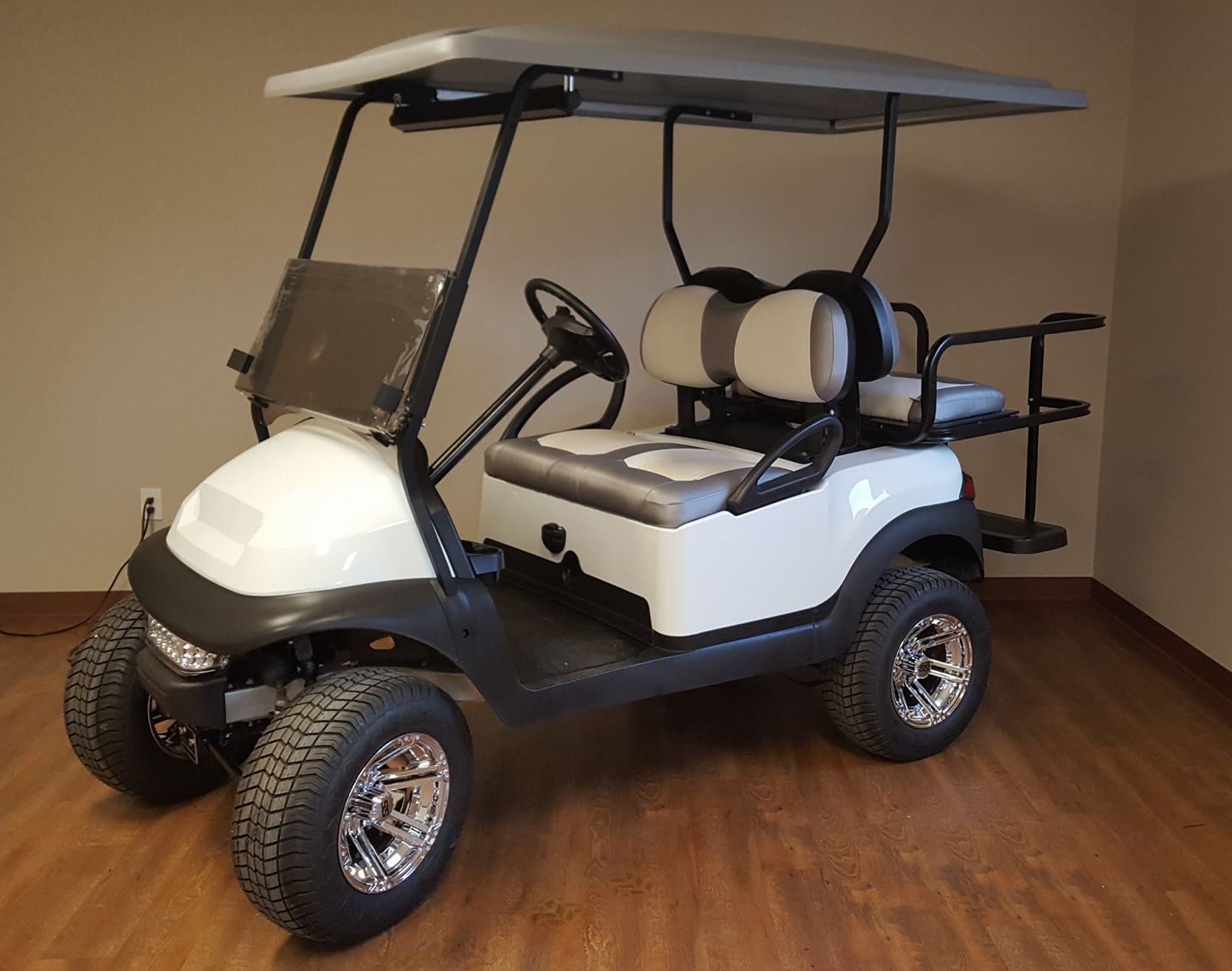 A white golf cart is parked on a wooden floor in a room.