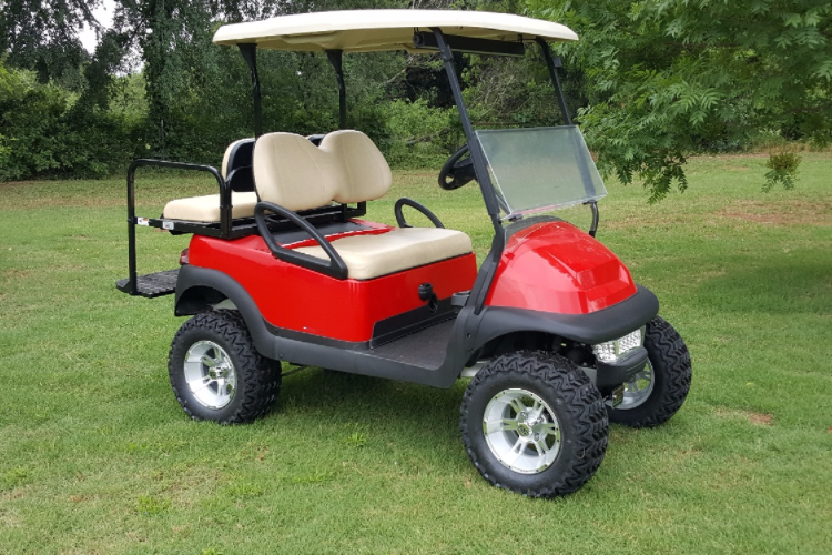 A red golf cart is parked on a lush green field.