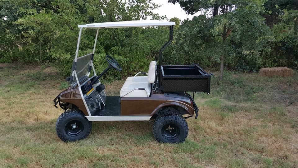 A brown and white golf cart is parked in a grassy field.