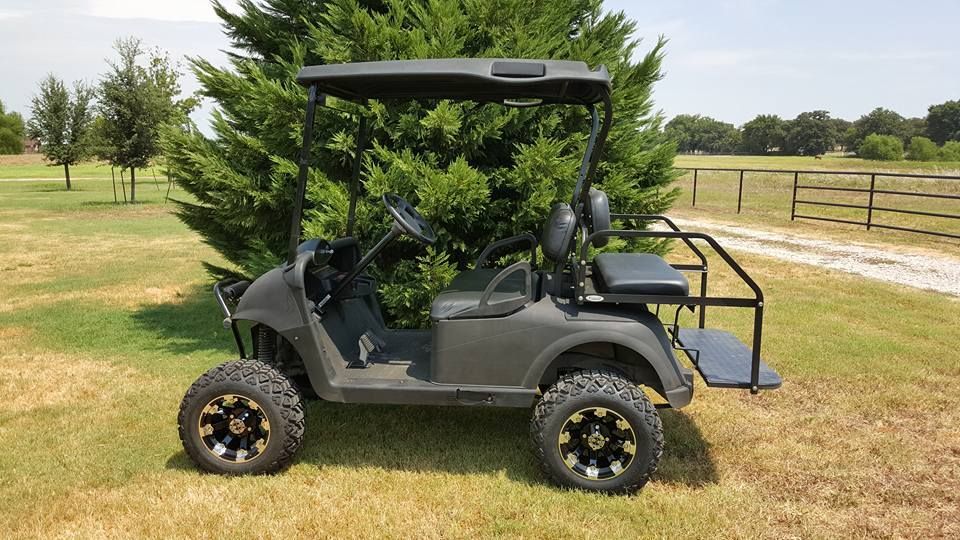 A black golf cart is parked in the grass next to a tree.