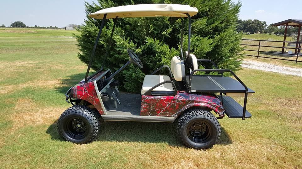 A red golf cart is parked in a grassy field next to a tree.