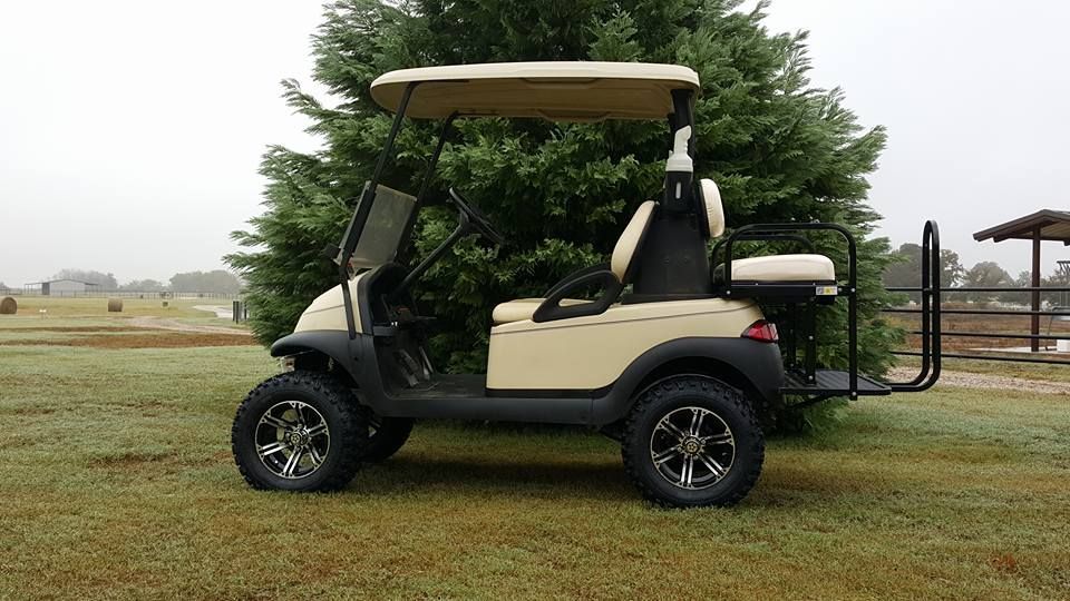 A golf cart is parked in a grassy field next to a tree