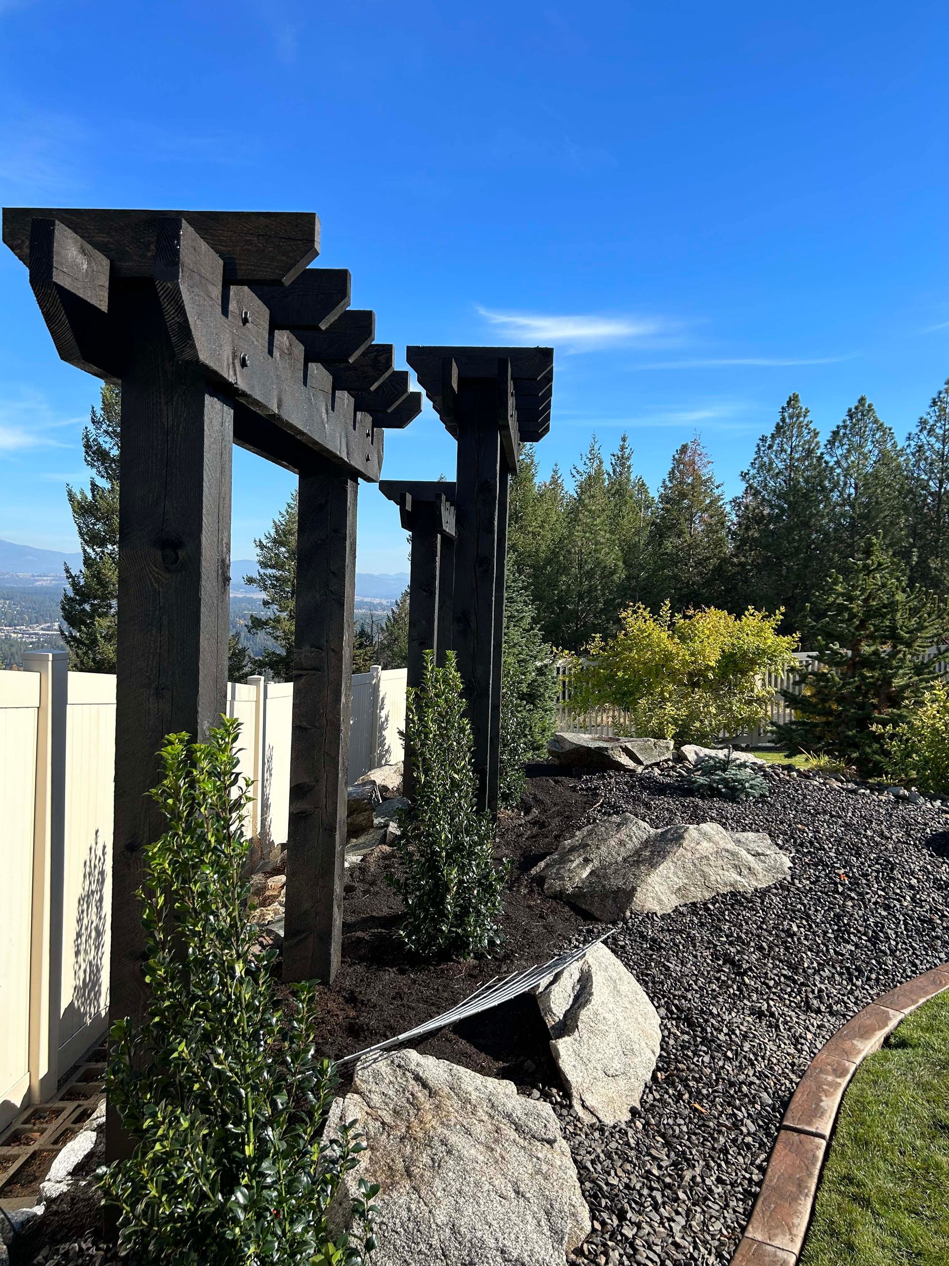 A wooden pergola is surrounded by rocks and bushes in a garden.