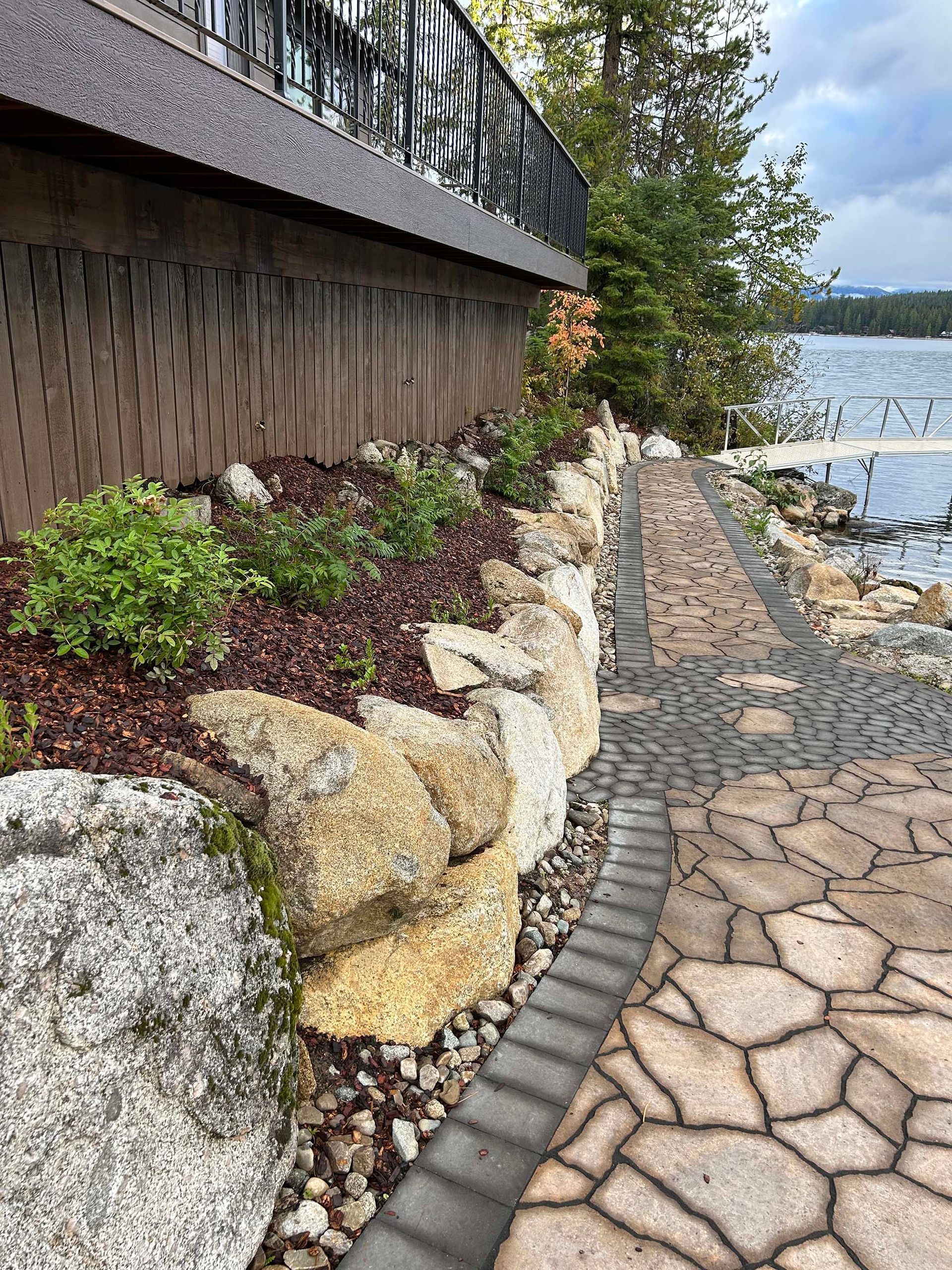 A stone walkway leading to a lake surrounded by rocks and plants.