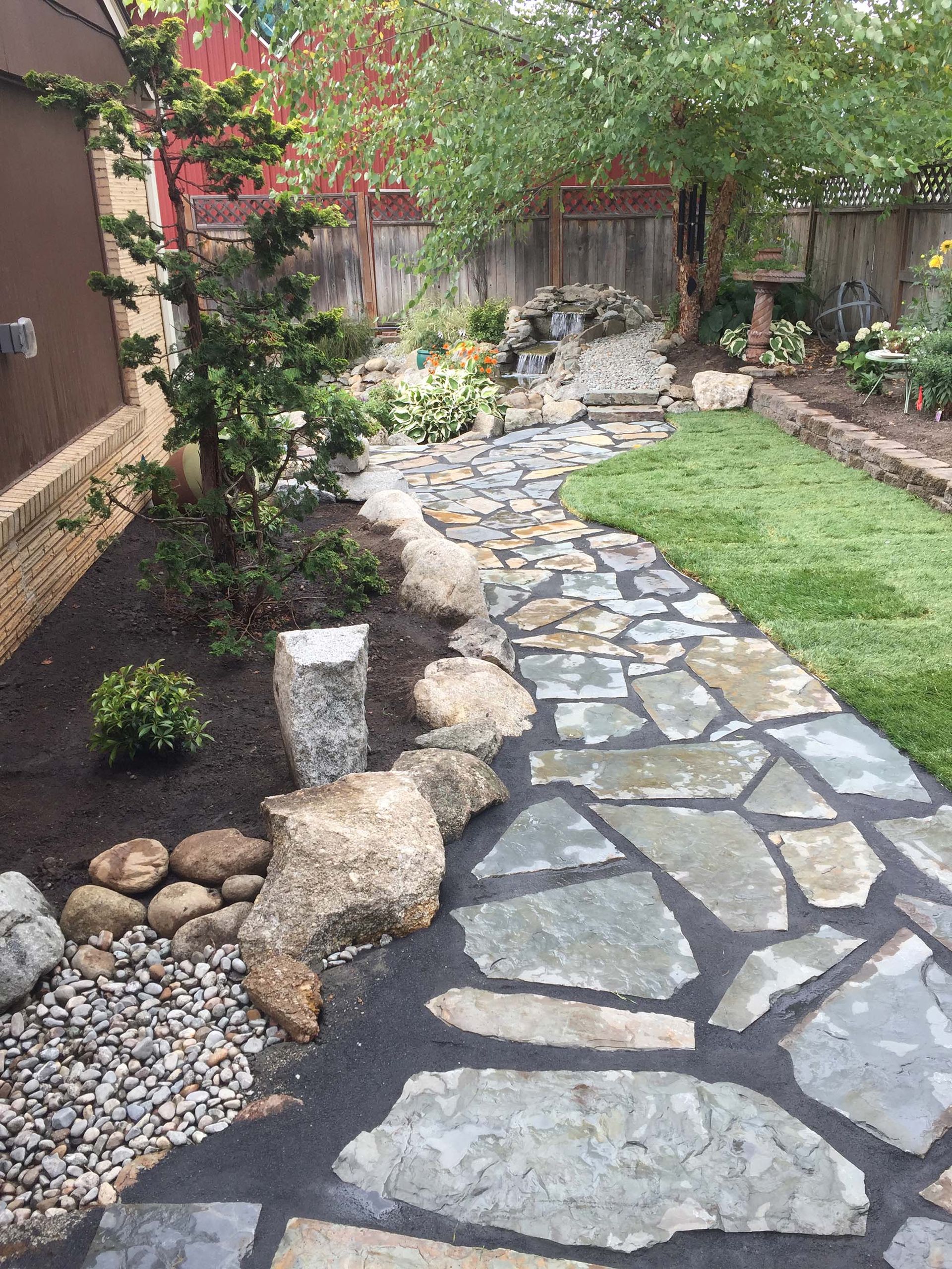 A stone walkway in a backyard surrounded by rocks and grass.