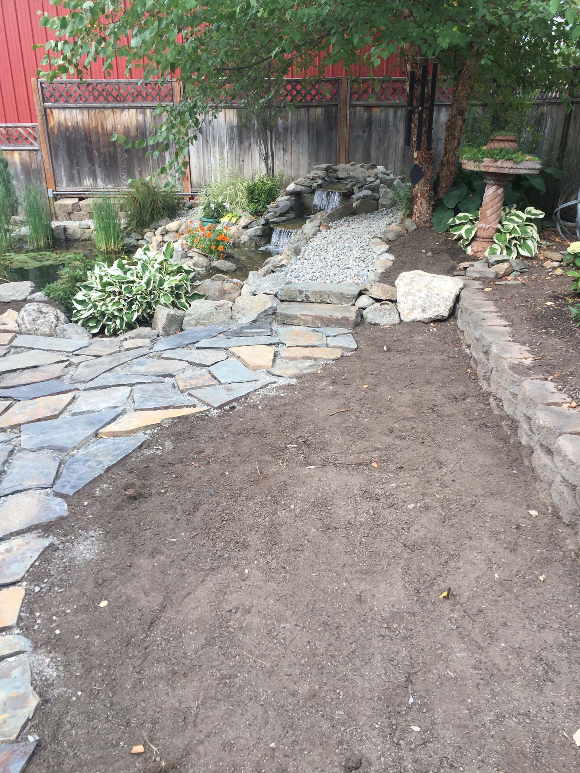 A stone walkway leading to a pond in a backyard.