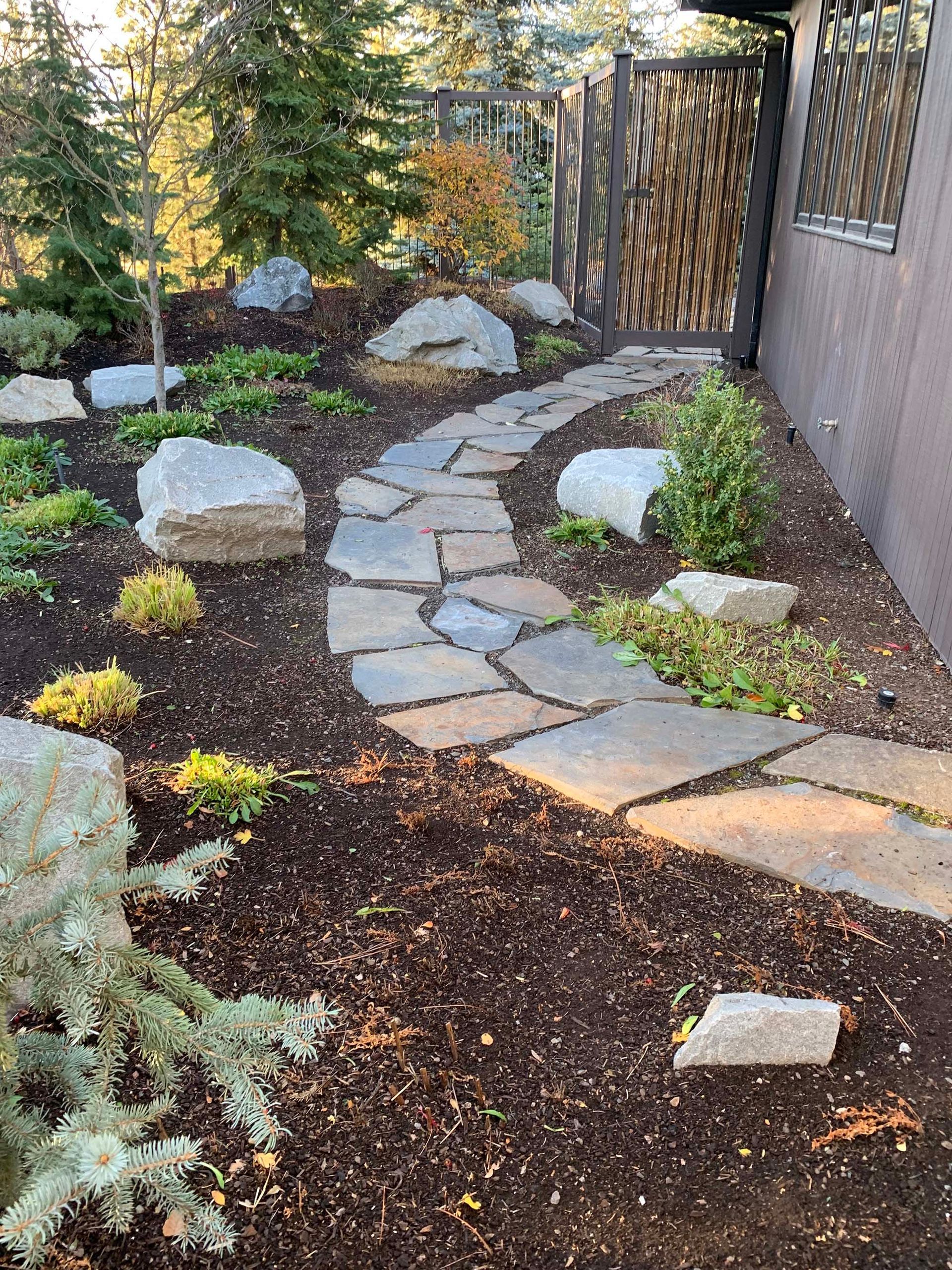 A stone walkway leading to a house in a garden.