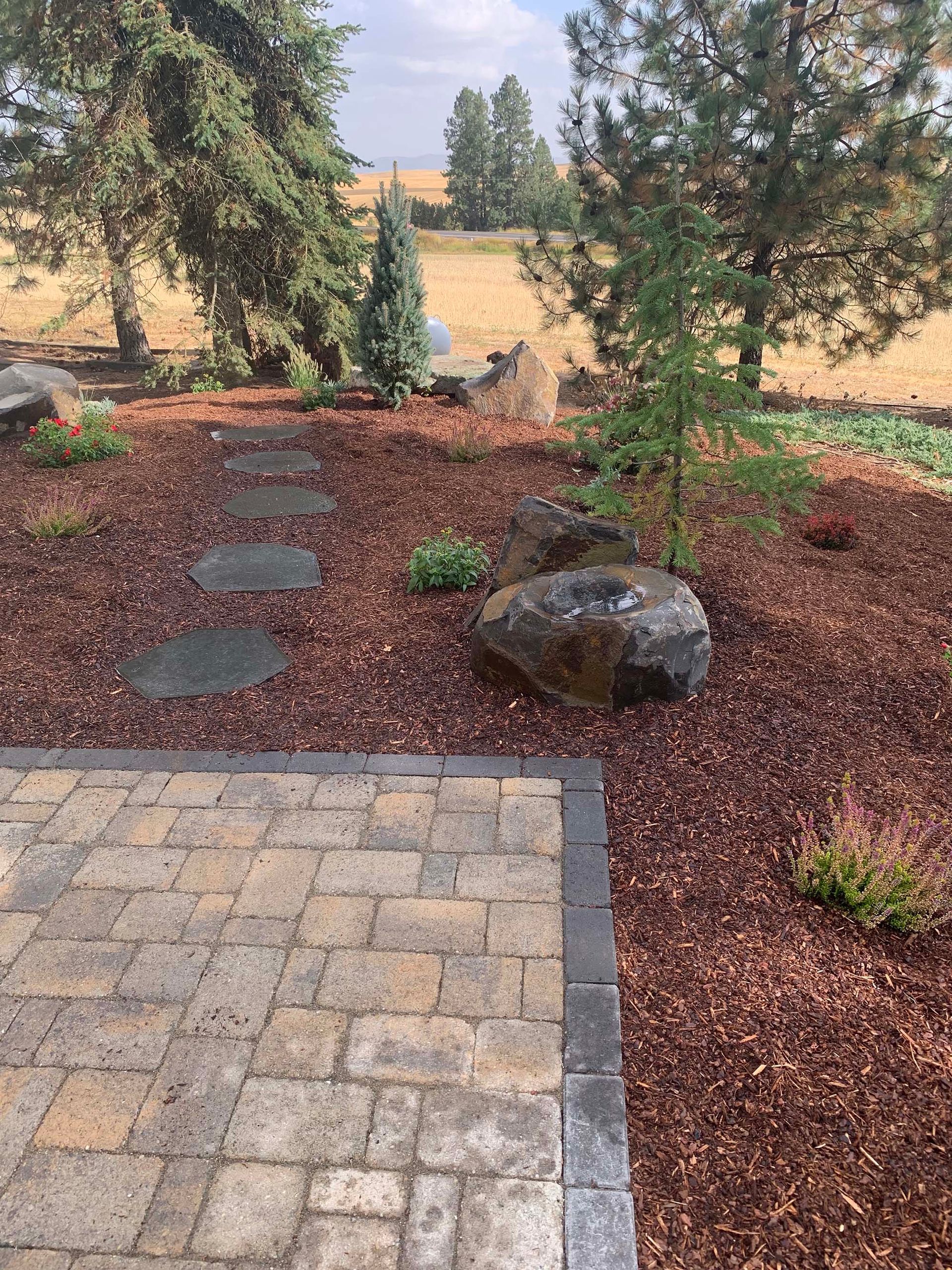 A stone walkway leading to a patio with trees in the background.
