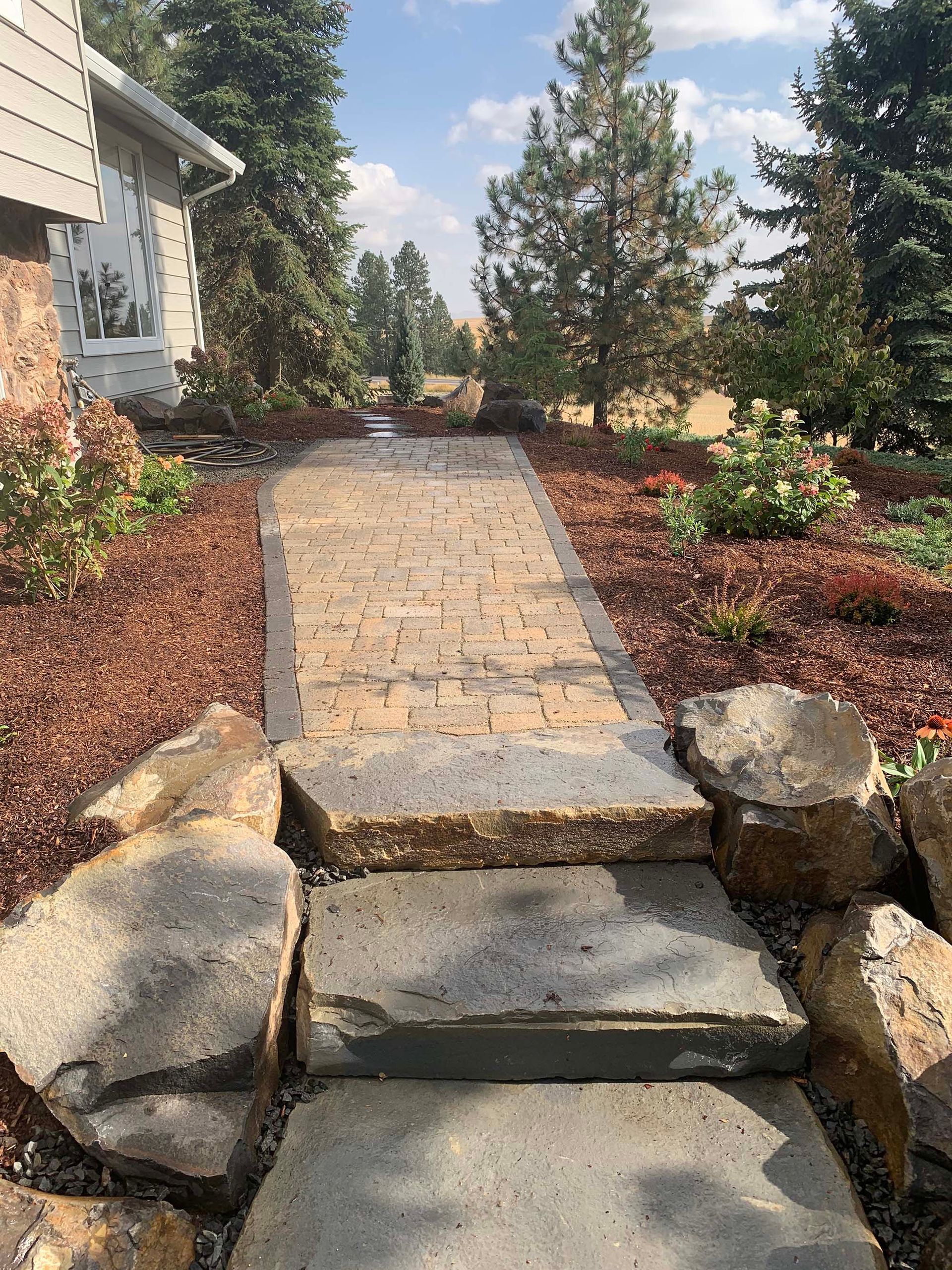 A stone walkway leading to a house surrounded by trees and rocks.