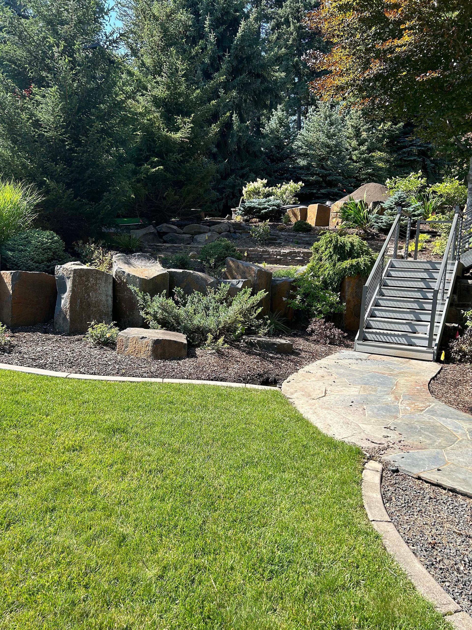 A lush green lawn with a stone walkway leading to a bridge.
