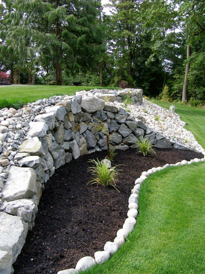 A large rock in the middle of a garden next to a fence.