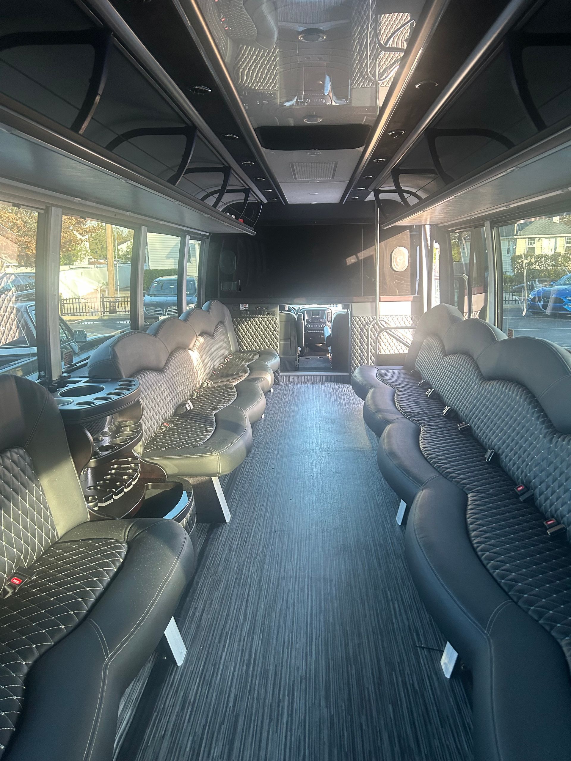 Interior of a bus with rows of black and patterned seats, dark flooring, and windows.