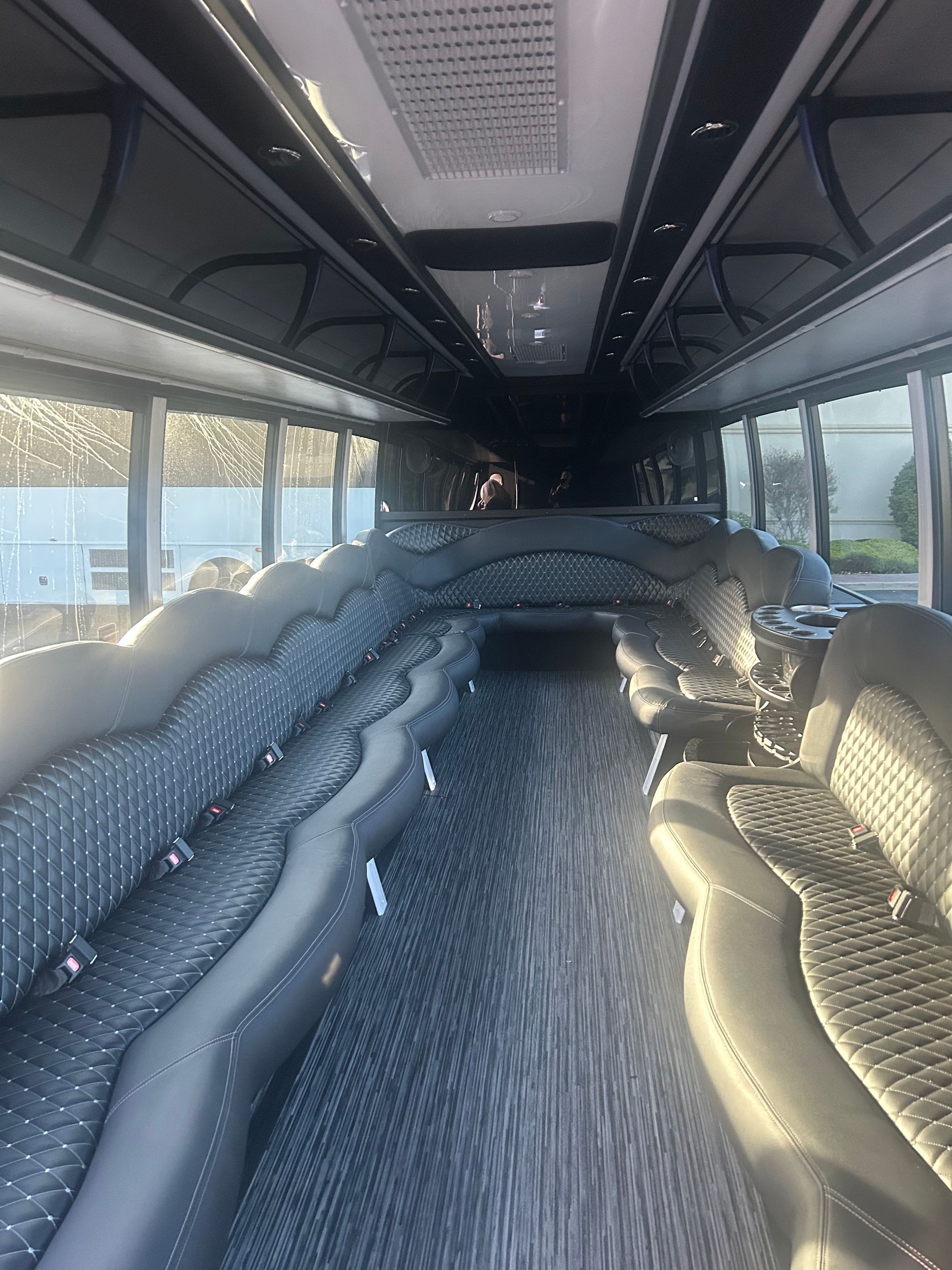 Interior view of a bus with rows of gray seating and a long, dark ceiling.