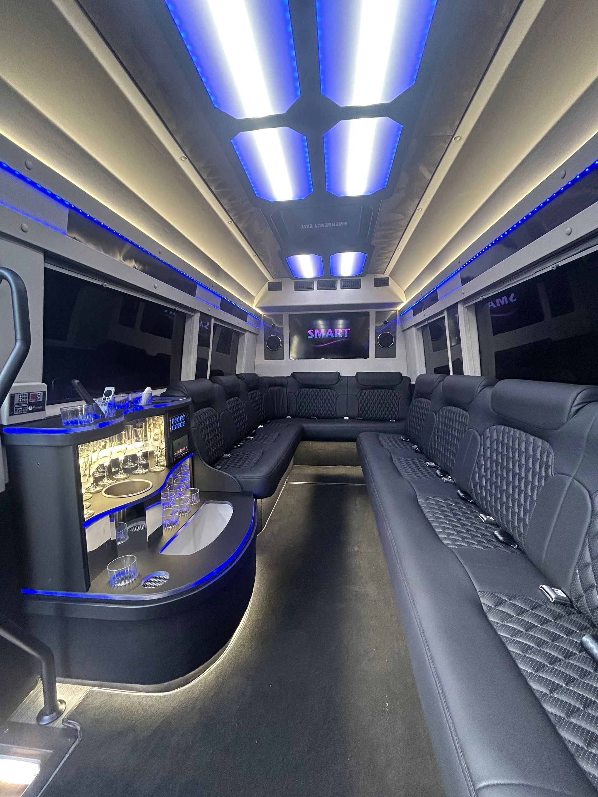 Inside a luxury party bus: black seating, bar, neon blue lights, and mirrored ceiling.