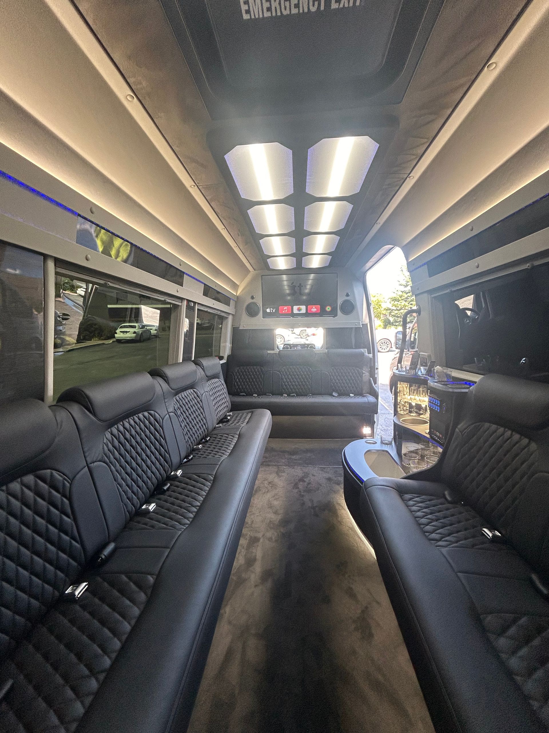 Interior of a luxury bus with black leather seating, overhead lighting, and a gray carpeted floor.