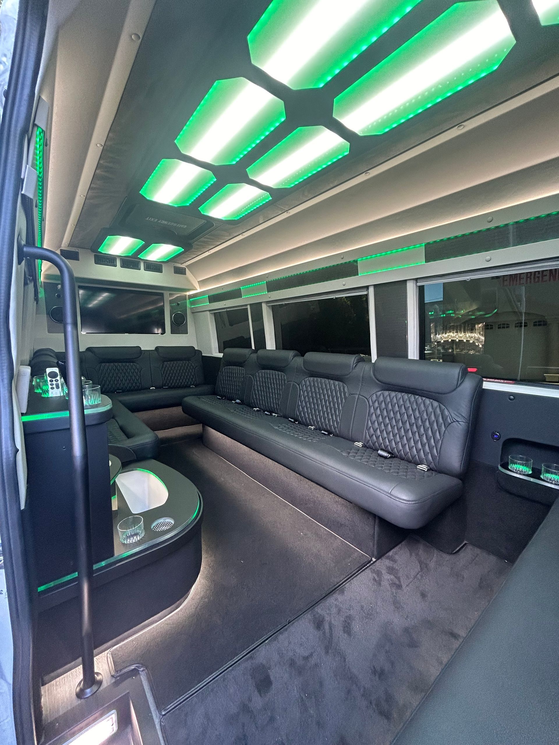 Interior of a party bus with black leather seating, green lighting, and a bar area.