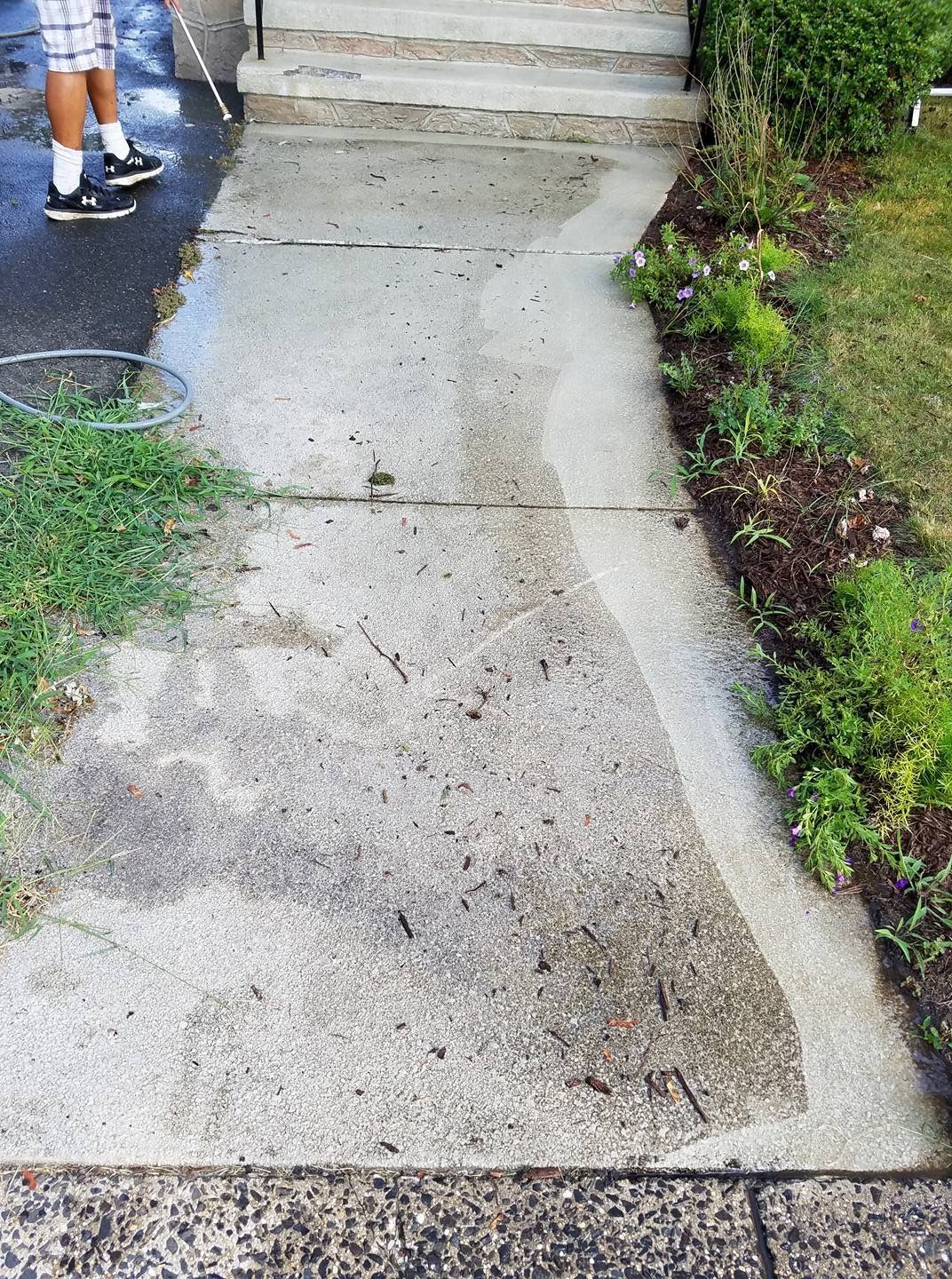 A person is cleaning a sidewalk with a pressure washer.