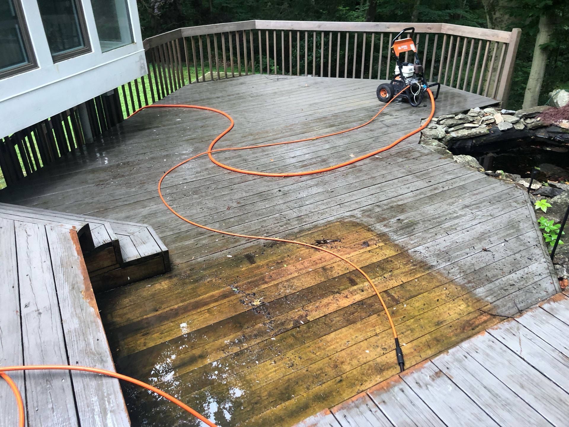 A person is cleaning a wooden deck with a pressure washer.