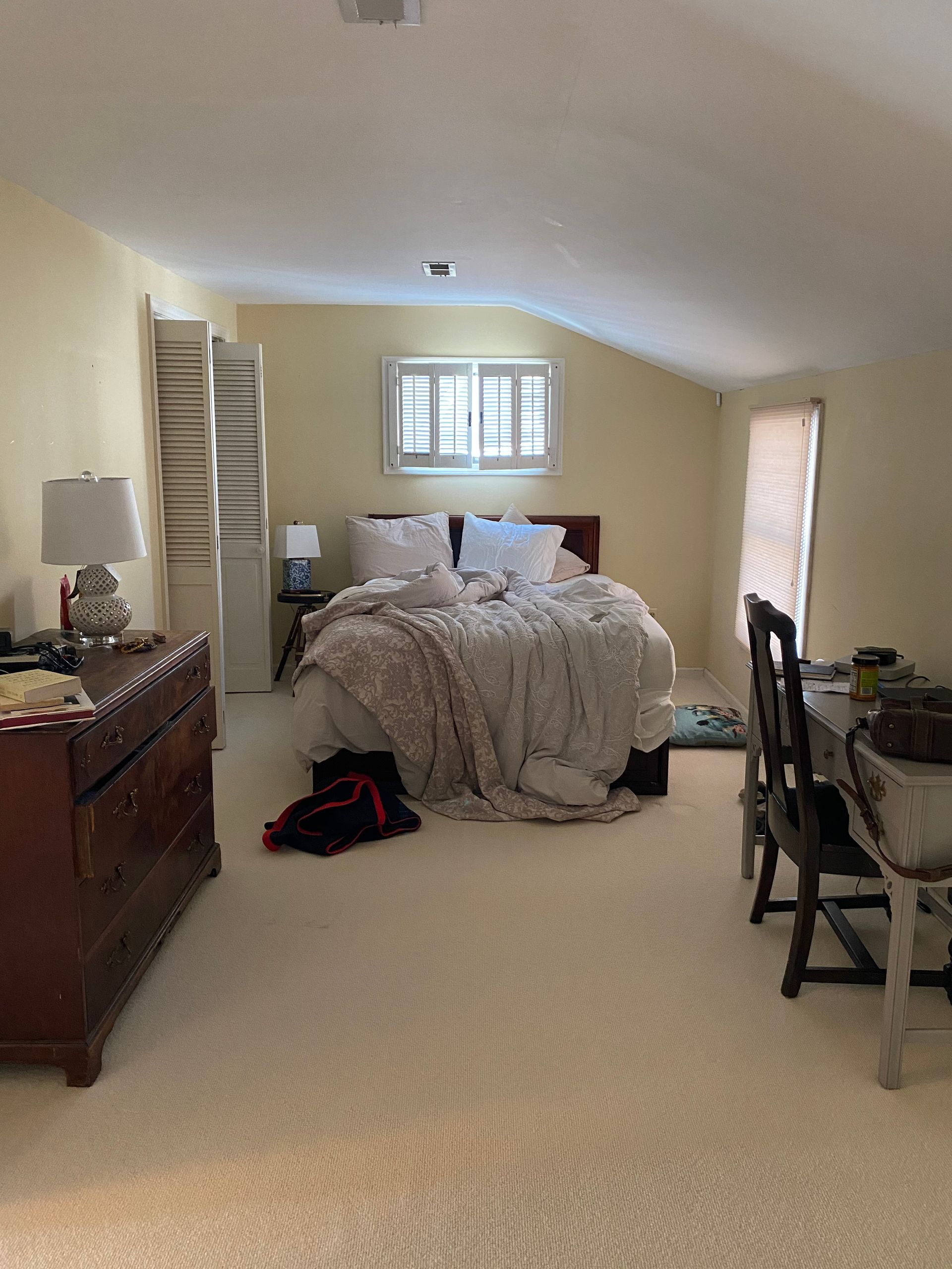 A bedroom with a bed, dresser, desk, and chairs.