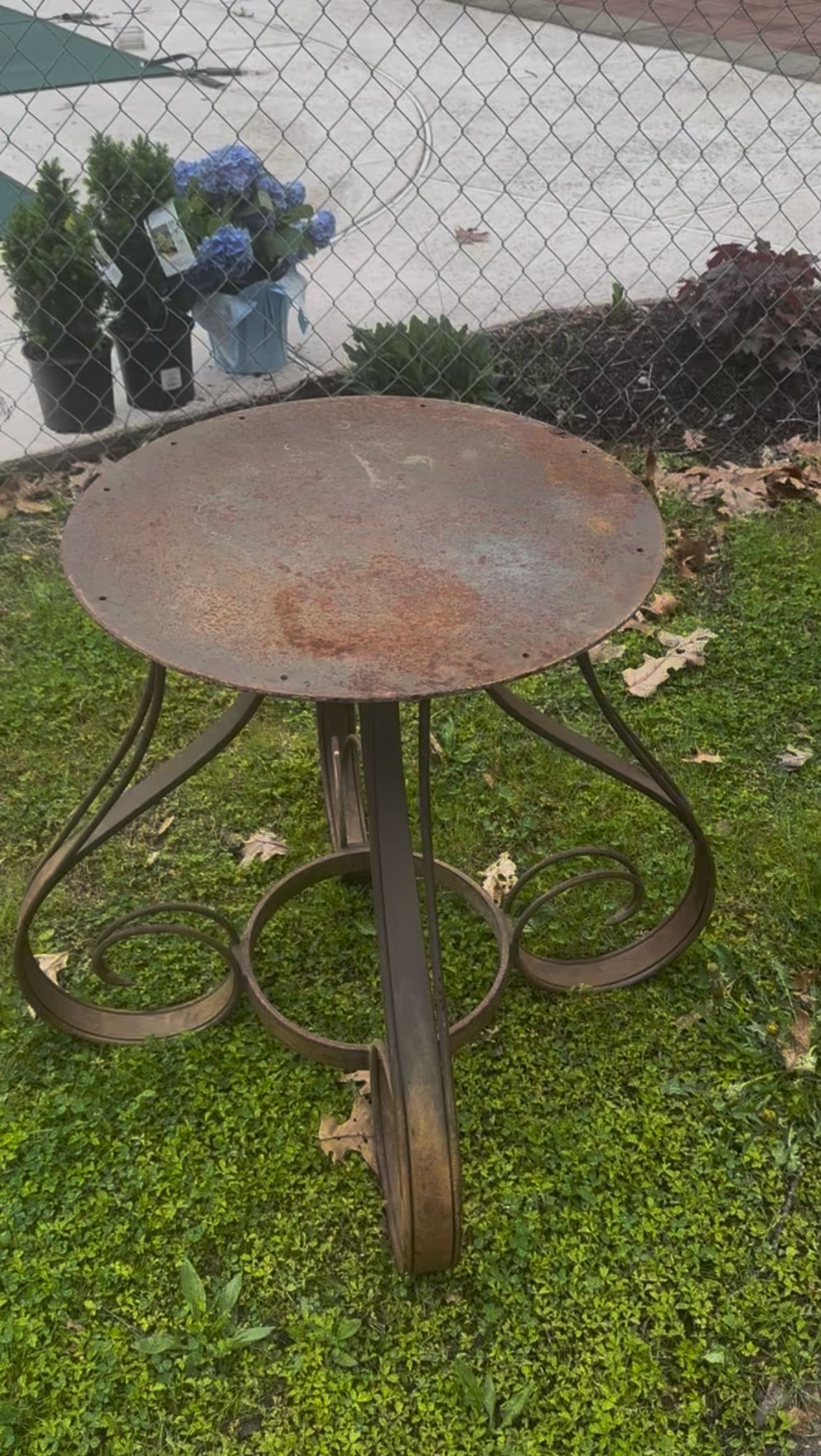 A rusty metal table is sitting in the grass next to a chain link fence.