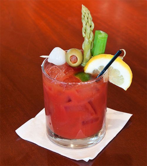 A Bloody Mary cocktail in a glass with garnishes including an olive, lemon slice, and asparagus, on a napkin.
