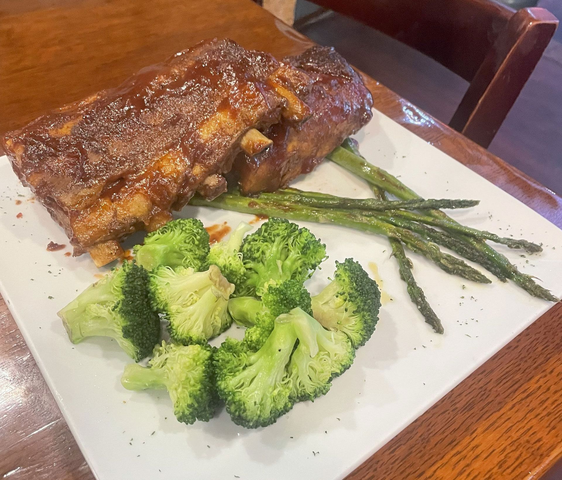 Grilled salmon fillet on a white plate with a side salad of tomatoes, cucumber, olives, and lemon.