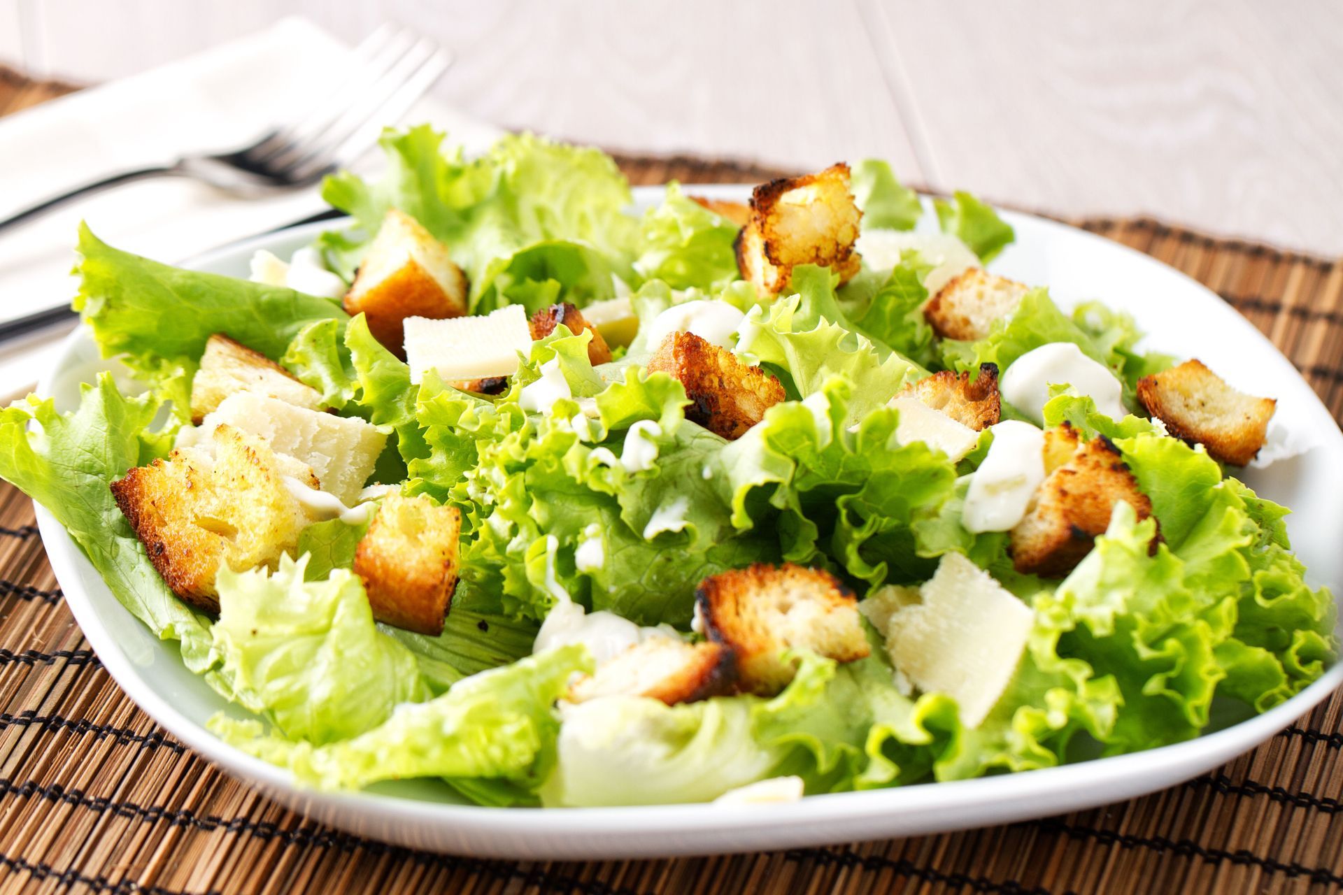 Caesar salad with lettuce, croutons, and cheese on a white plate, resting on a bamboo mat.