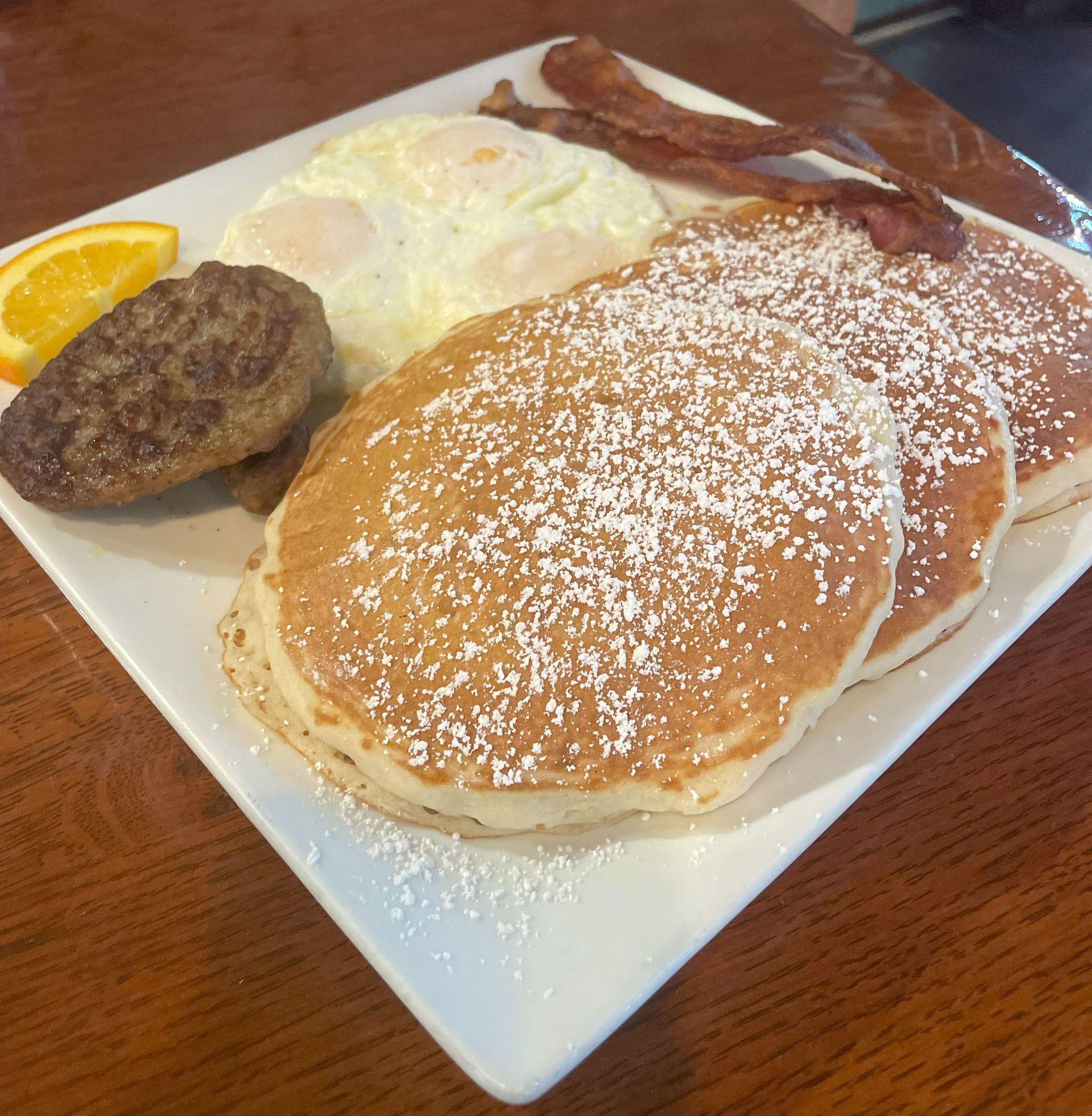Stack of golden pancakes topped with a pat of butter, on a light orange plate.