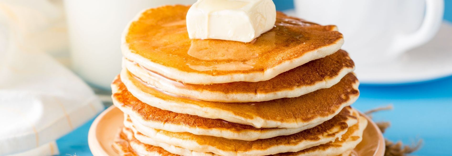 Stack of golden pancakes topped with a pat of butter, on a light orange plate.