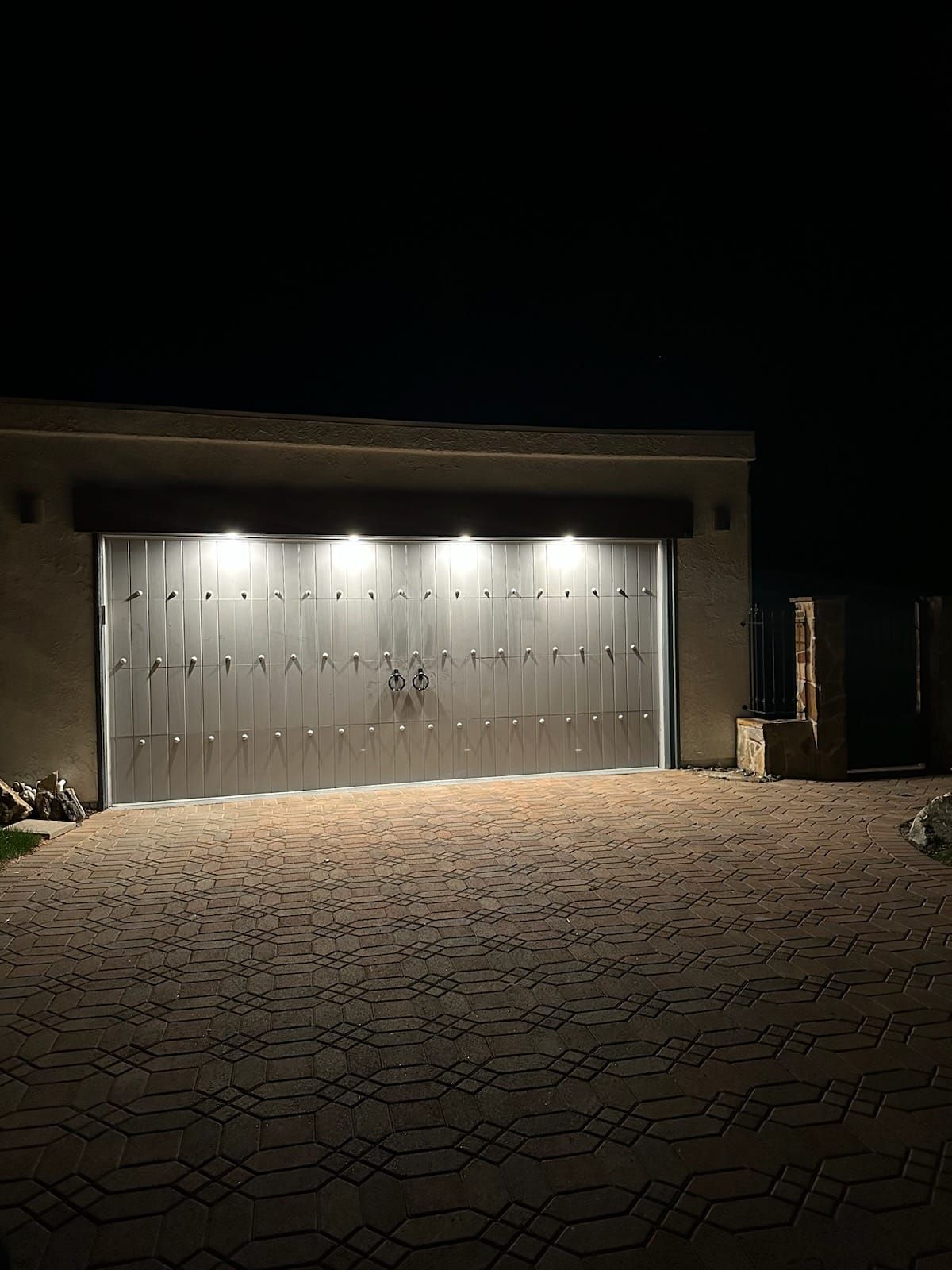 Garage door illuminated at night, with a brick driveway.