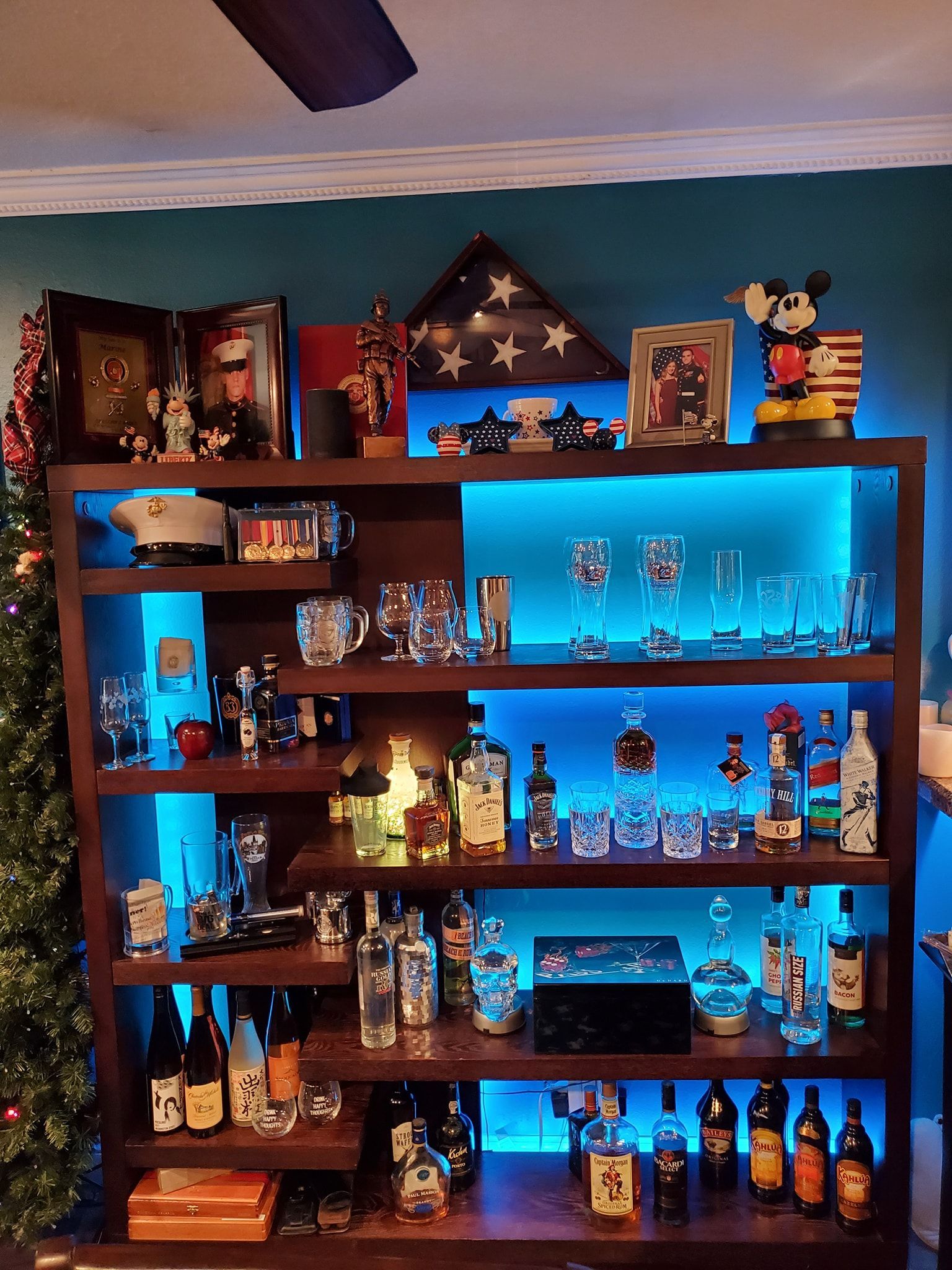 Wooden bar shelf with blue LED backlighting, displaying bottles, glassware, and decorations.