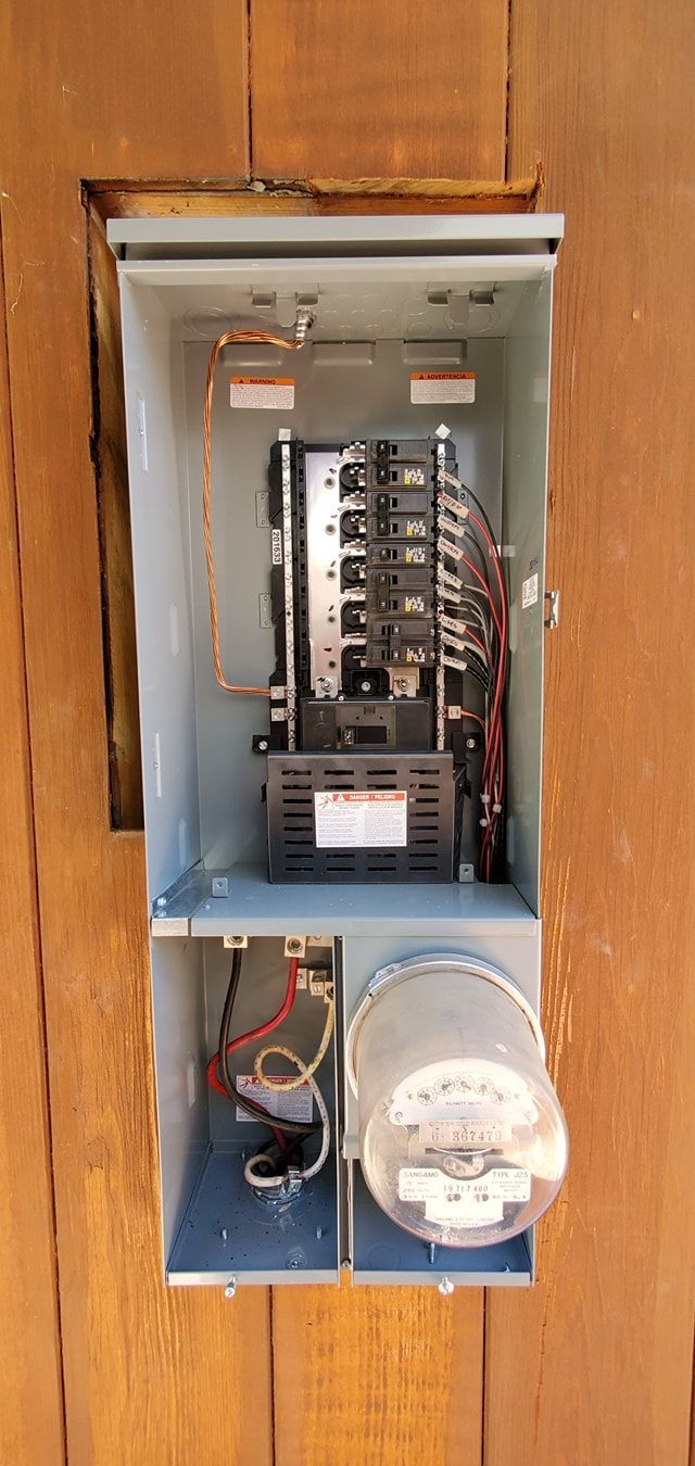 Electrical panel installed in a wooden wall with circuit breakers, wires, and a meter.