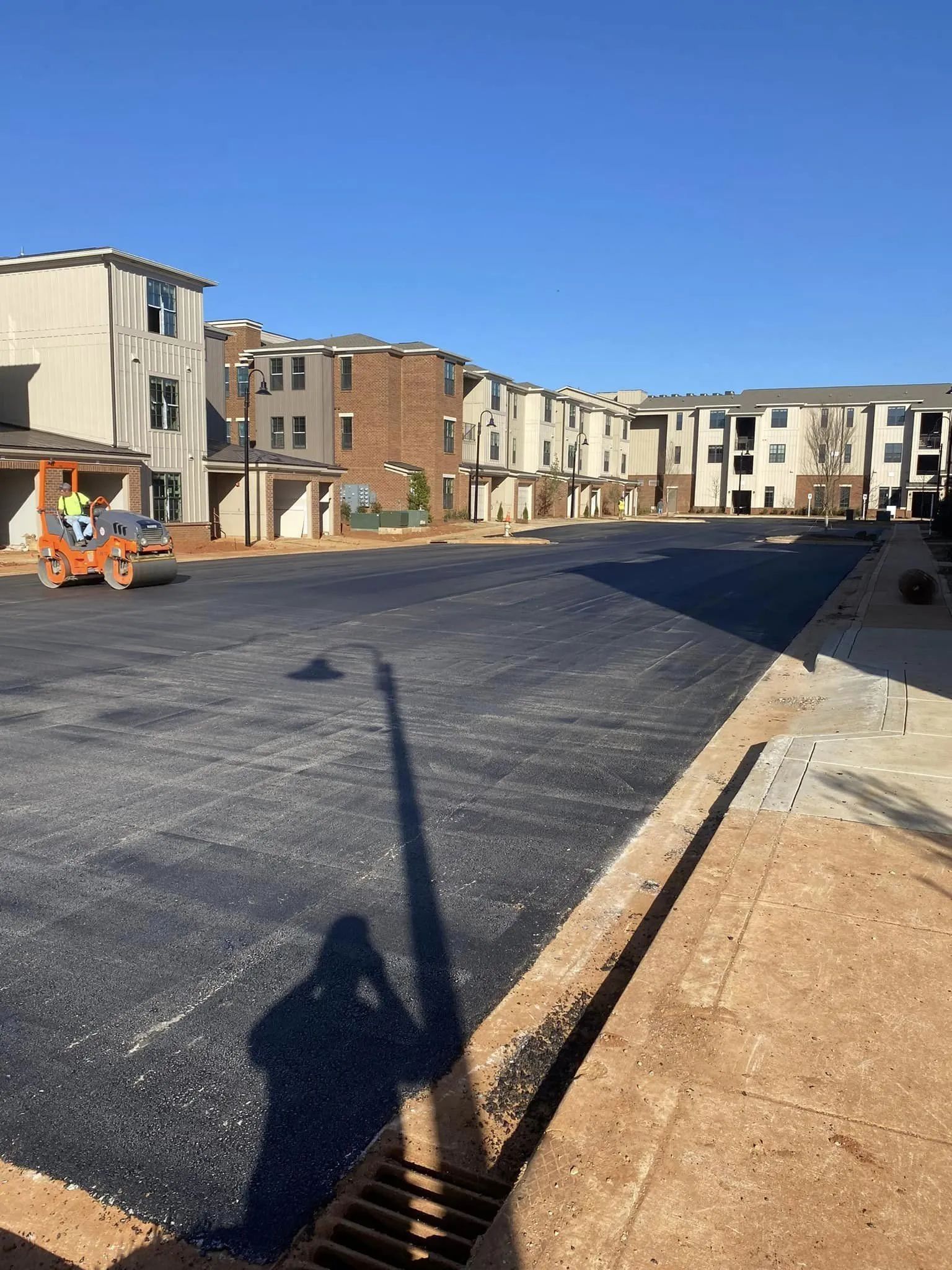 A bright, sunny day at a construction site with a freshly paved asphalt parking lot and a steamroller in the distance.
