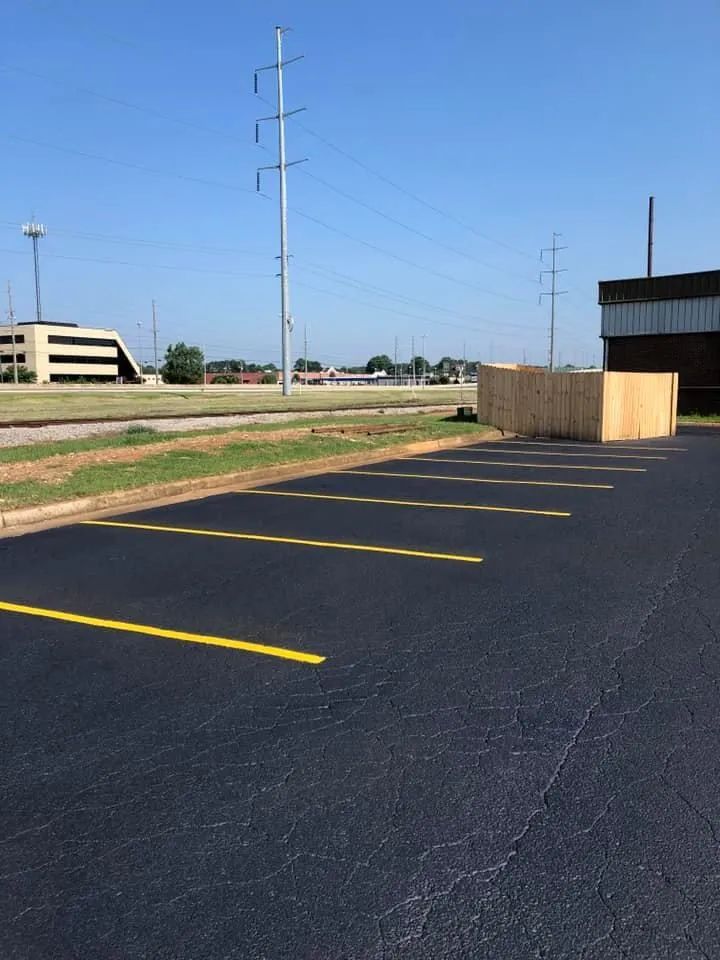 A freshly paved asphalt parking lot with bright yellow painted lines, under a clear blue sky.