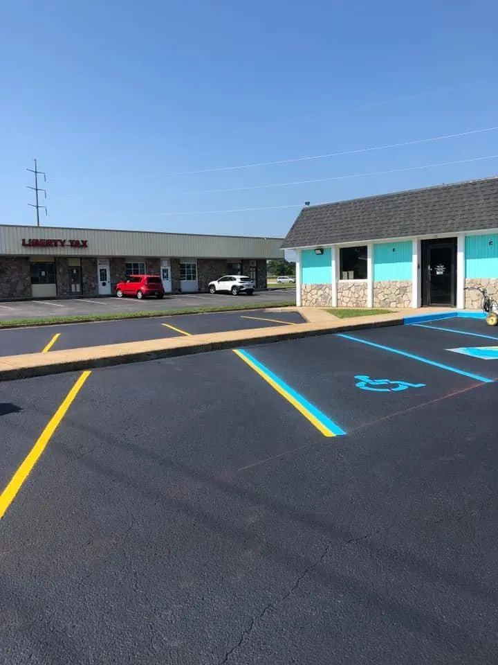 A parking lot with a handicap-accessible spot in the foreground, next to a teal-colored building and a strip mall.