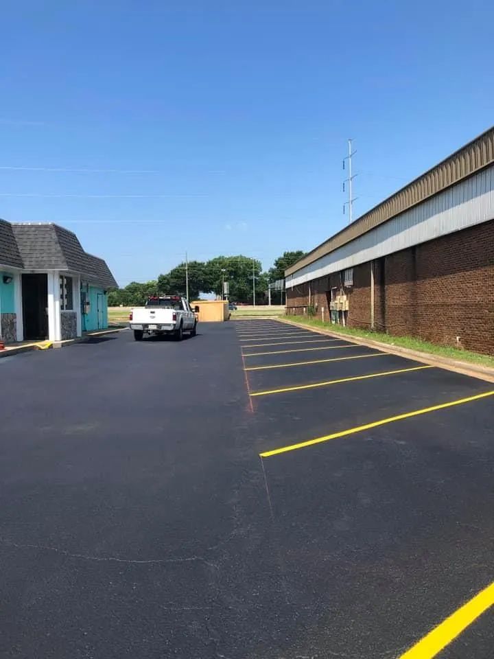 A freshly paved asphalt parking lot with yellow painted lines next to a brick building and a white truck.