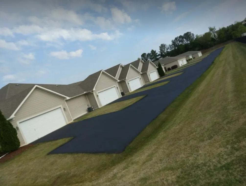 A row of beige suburban houses with white garage doors and a newly paved dark asphalt driveway.