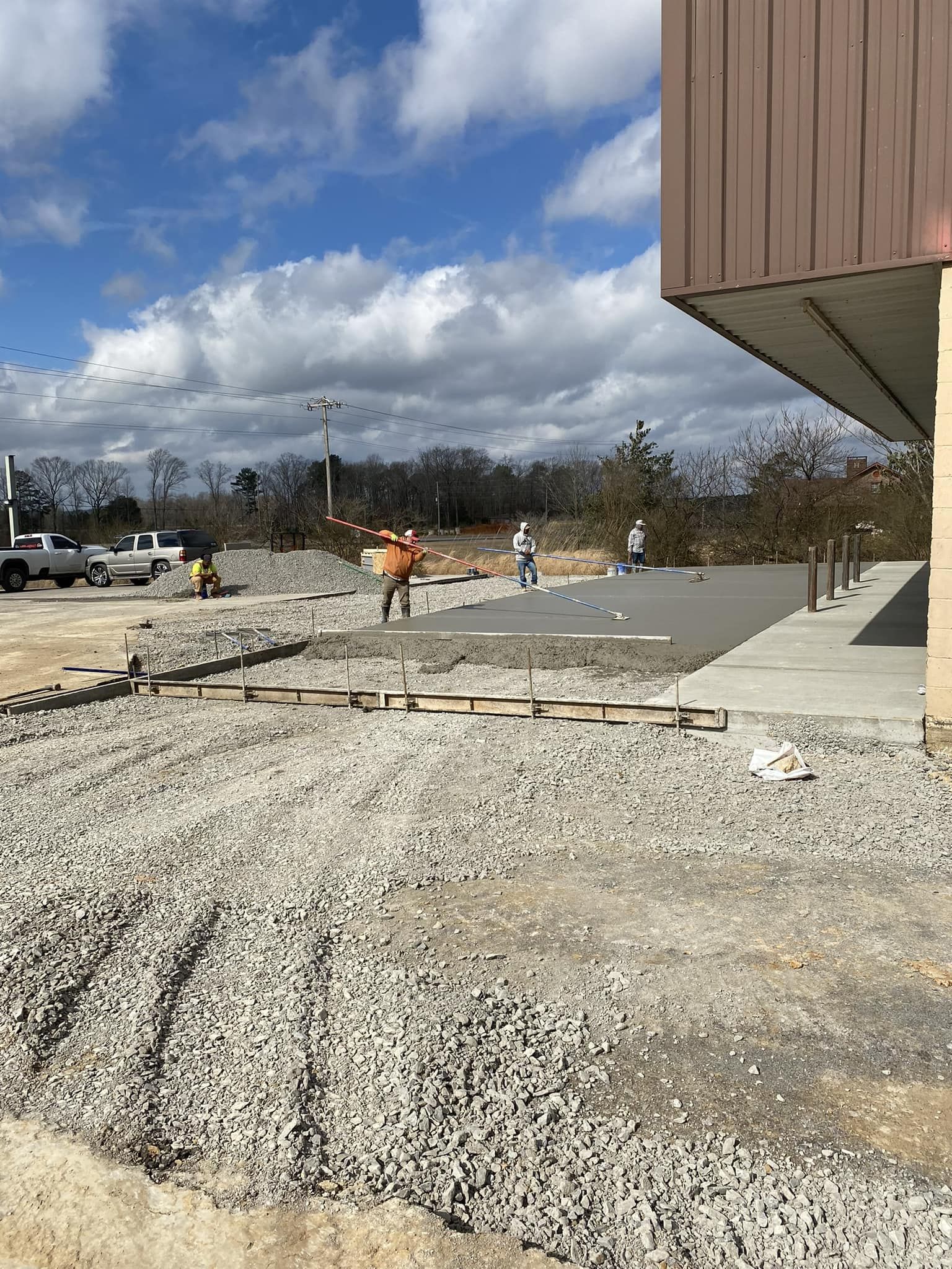 Construction workers smoothing wet concrete for a new sidewalk alongside a building on a sunny day.