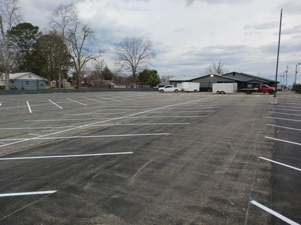 A wide, outdoor parking lot with freshly painted white parking stripes on asphalt under a cloudy sky.