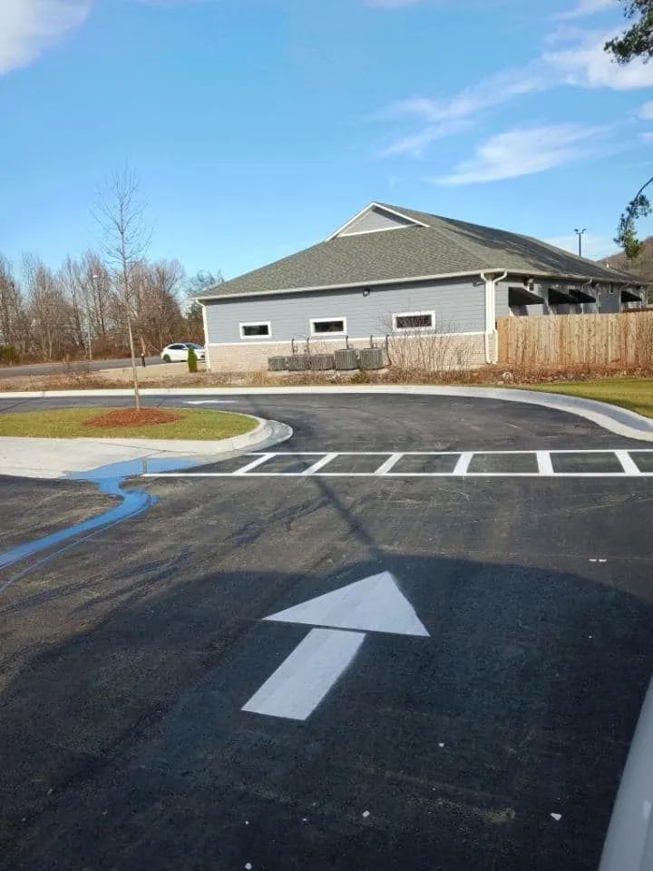 A paved driveway with a white directional arrow and a pedestrian crosswalk leading toward a modern building.